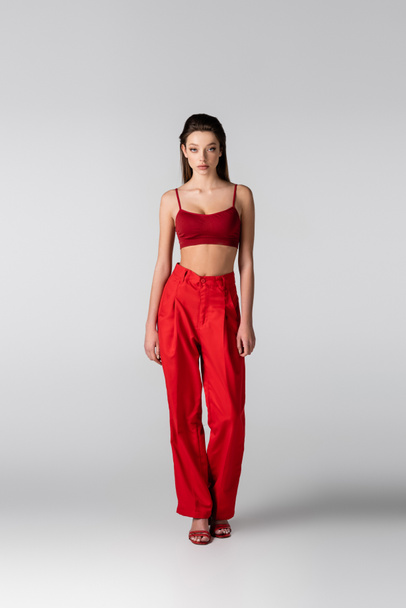 full length of model in red crop top and pants posing on grey - Zdjęcie, obraz