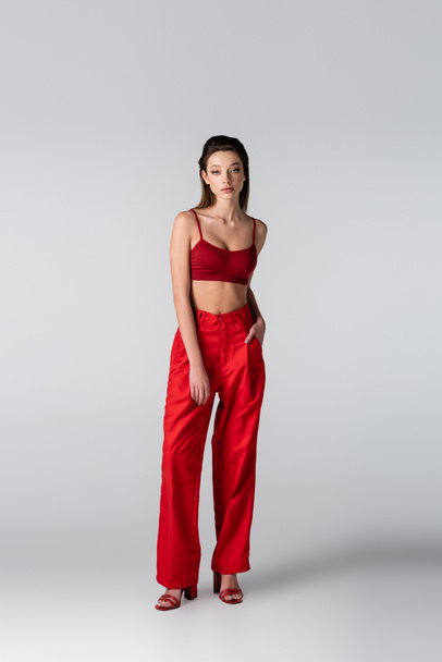 full length of model in red crop top and pants posing with hand in pocket on grey - Photo, image