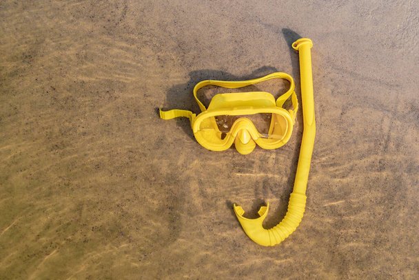 Yellow underwater waterproof mask with a diving snorkel in the water on the seashore with a sandy bottom. Top view, close-up - Valokuva, kuva