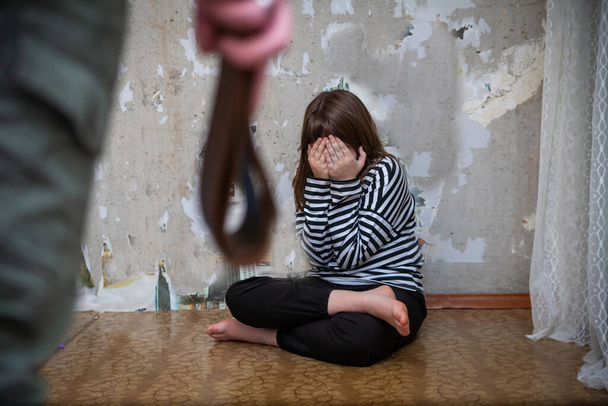 Retrato de adolescente asustada sentada contra la pared hombre agresivo opuesto con cinturón en la mano.  - Foto, Imagen