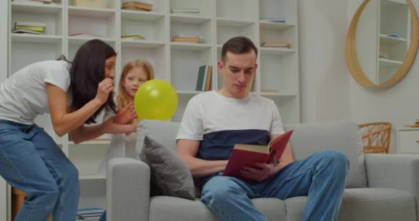 Niña con madre asustando a su padre reventando globo. Broma del Día de los Inocentes - Imágenes, Vídeo