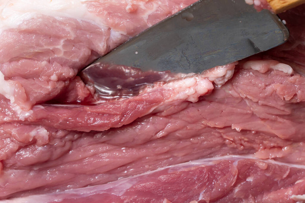 Szeletelje fel a sertést vagy a marhahúst egy késsel az asztalon közelről. Húsételek és élelmiszeripari termékek.Piros húsdarabok a shish kebab, barbecue vagy kebab számára.Nyers friss húst késsel vágunk.Recept - Fotó, kép