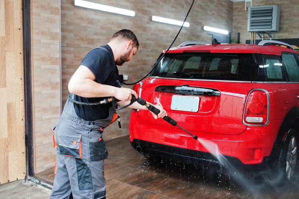 Man worker washing red car in detailing garage. - Zdjęcie, obraz