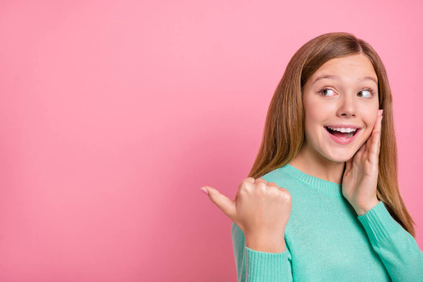 Фото солодкої збудженої школярки, одягненої в сльозогінний пуловер, що вказує на порожній простір рук щоки ізольований рожевий колір фону
 - Фото, зображення