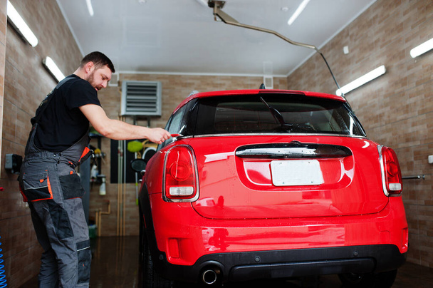 Man worker washing red car in detailing garage. - Φωτογραφία, εικόνα