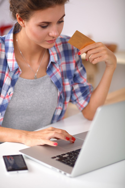 Χαμογελαστή γυναίκα online ψώνια χρησιμοποιώντας υπολογιστή και πιστωτική κάρτα στην κουζίνα - Φωτογραφία, εικόνα