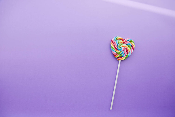 Arco iris colorido corazón en forma de caramelo sobre fondo púrpura con sombras. Copiar espacio. Concepto minimalista. - Foto, imagen
