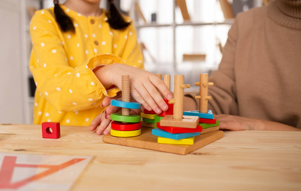 una bambina è seduta a un tavolo e gioca un giocattolo di legno in via di sviluppo. Sviluppo del bambino - Foto, immagini