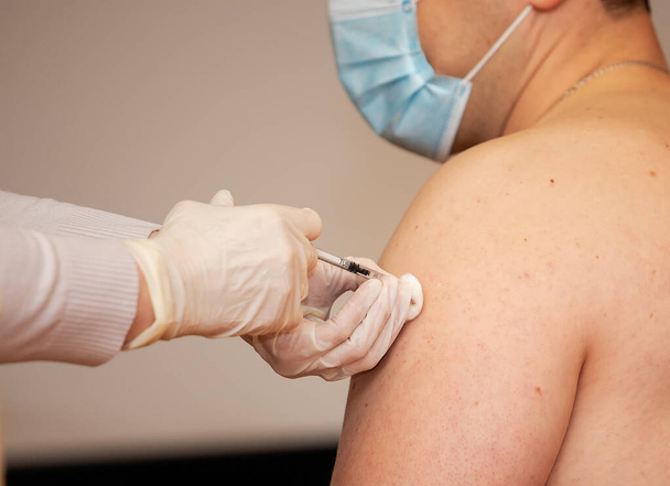 A person is injected with a syringe in the shoulder. Coronavirus vaccine. Vaccination and treatment of dangerous infections. - Фото, изображение
