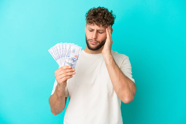 Nuori valkoihoinen mies ottaa paljon rahaa eristetty sinisellä taustalla päänsärky - Valokuva, kuva