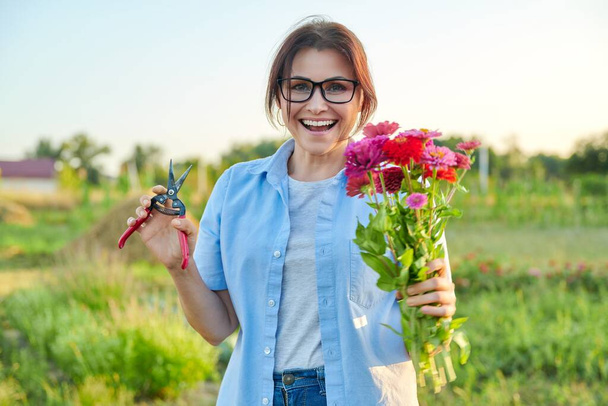 Smiling middle aged female holding bouquet of fresh zinnia flowers in garden - Foto, immagini