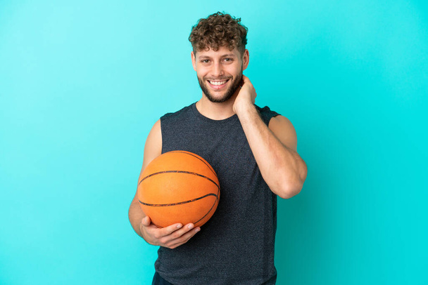 Basketbol oynayan yakışıklı genç adam mavi arka planda izole edilmiş gülüyor. - Fotoğraf, Görsel