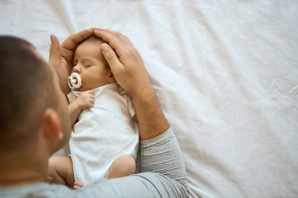 Close-up van een onherkenbare vader met een hoofd van een slapende baby, slapend in een bed. In de veilige handen - Foto, afbeelding