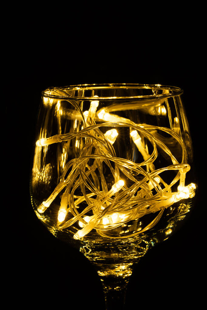 Luz de fada em um copo de vinho, no escuro, Fotografia Low-Key. - Foto, Imagem