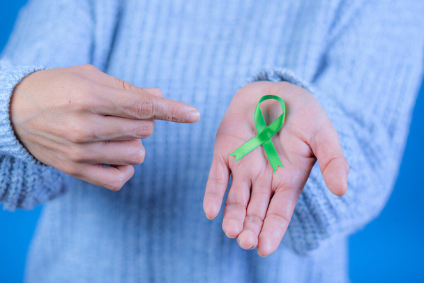 Groen lint ter ondersteuning van het bewustzijn van leverkanker en bijnierkanker, mensenhanden met groen lint. Wereldkankerdag. Ruimte voor tekst - Foto, afbeelding