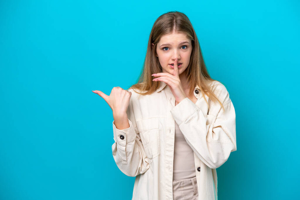 Teenager Russian girl isolated on blue background pointing to the side and doing silence gesture - Photo, Image