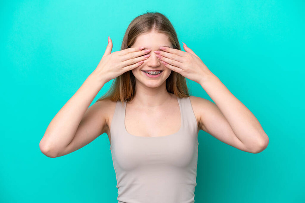 Teenager Russian girl isolated on blue background covering eyes by hands and smiling - Foto, Bild