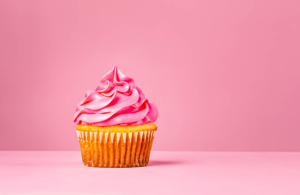Pinkfarbener Cupcake mit Buttercreme-Zuckerguss auf rosa Hintergrund. - Foto, Bild