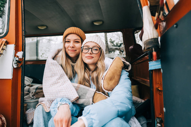 Portret van twee vrolijke jonge vriendinnen in een busje in winterkamp. - Foto, afbeelding