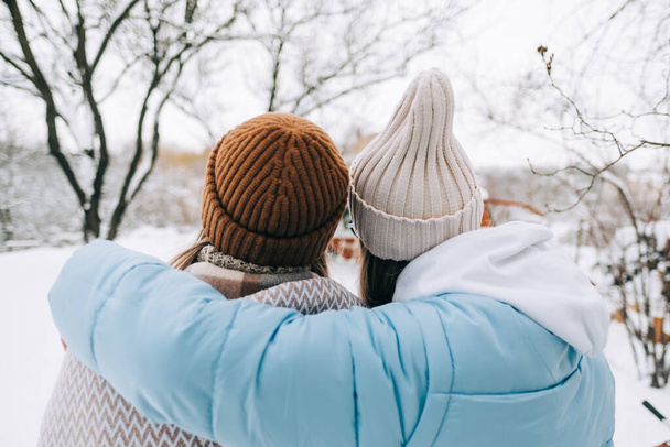 Two sisters standing in the backyard and hugging, looking around after snowfall in the morning in winter time. - Foto, afbeelding