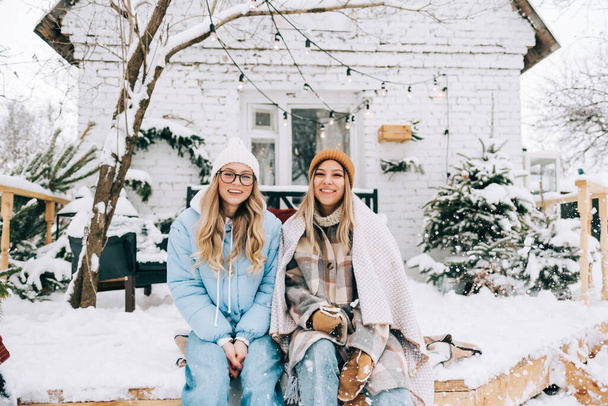 Portrait of two cheerful women friends sitting outdoor on the backyard after snowfall, enjoying winter time. - Photo, Image
