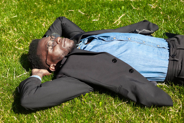 Joyful happy african office worker relaxing on grass in a summer park after a hard working day in the office - Foto, immagini