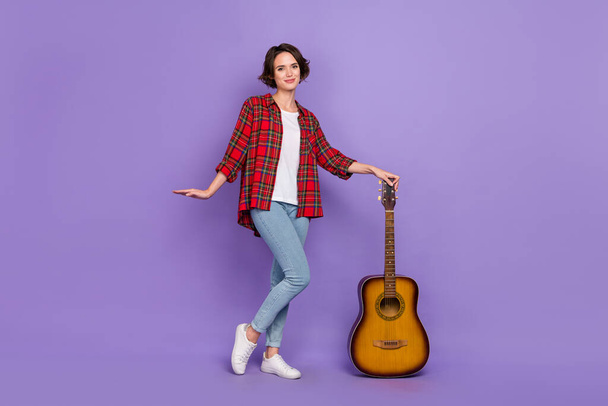 Full size photo of nice millennial brunette lady stand with guitar wear shirt jeans sneakers isolated on purple color background - Foto, Imagen