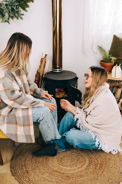 Two caucasian woman friends sitting near fireplace at home and having fun. - Foto, imagen