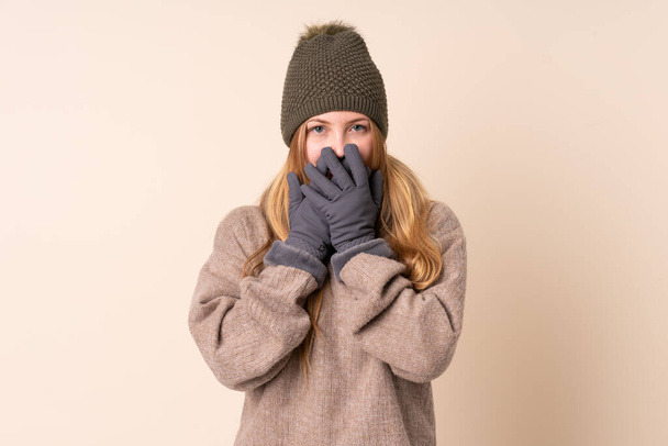 Підлітня українська дівчина з зимовим капелюхом ізольована на бежевому фоні з несподіваним виразом обличчя. - Фото, зображення