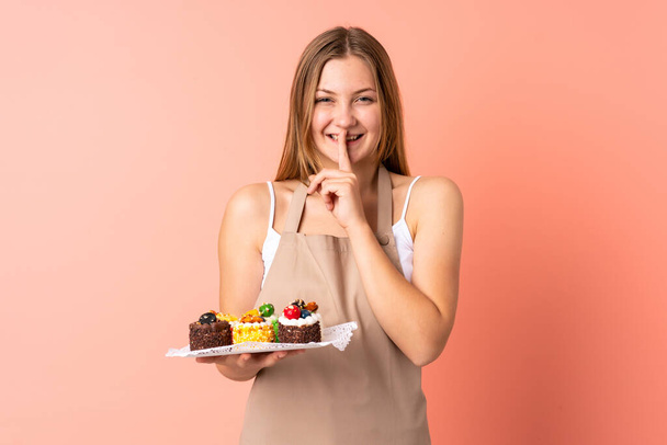 Pastry Ukrainian chef holding a muffins isolated on pink background doing silence gesture - Fotoğraf, Görsel
