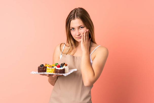 Ukraynalı pasta şefi pembe arka planda izole edilmiş bir kek tutuyor mutsuz ve hayal kırıklığına uğramış. - Fotoğraf, Görsel