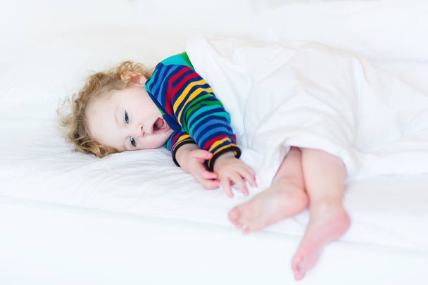 Смішна дівчинка позіхання малюка приймає серветку в білому ліжку
 - Фото, зображення