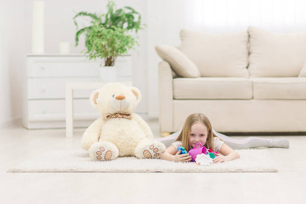 Photo of blond girl looking at the camera laying on the floor with toys. - Photo, Image