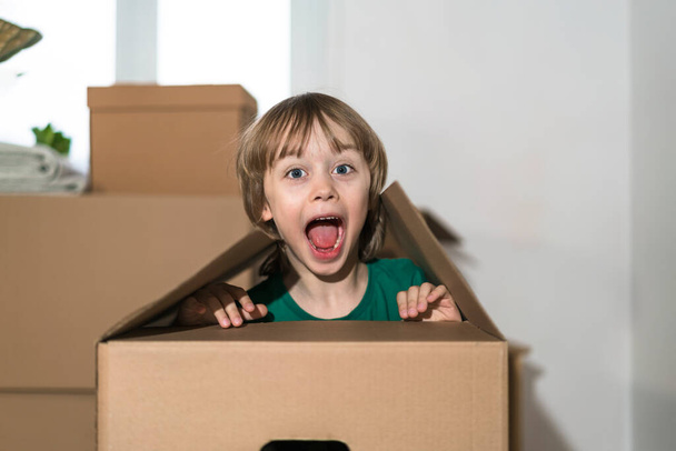 Cute toddler boy playing in cardboard box at new home. - Zdjęcie, obraz