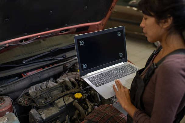 Jonge vrouw met laptop staan in de voorkant van open motorkap van de auto - Foto, afbeelding