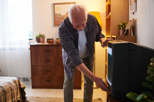 Senior man bending by tv set while switching it on or off - Foto, afbeelding