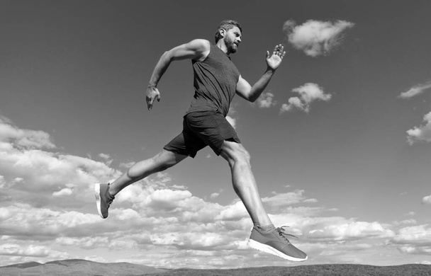 スポーツマンは空を背景にスポーツウェアの屋外で走る筋肉質の体で飛び回る、スタミナ. - 写真・画像