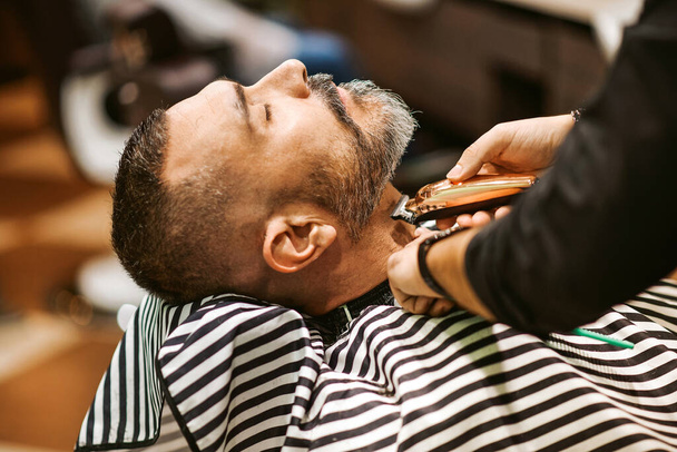 Barbiere taglia la barba del cliente nel suo negozio di barbiere in un concetto di bellezza e cura - Foto, immagini