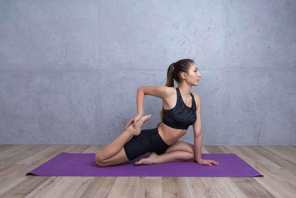 Mladá žena cvičí jógu při cvičení doma během karantény. Minimalistický prázdný interiér, betonová stěna. - Fotografie, Obrázek