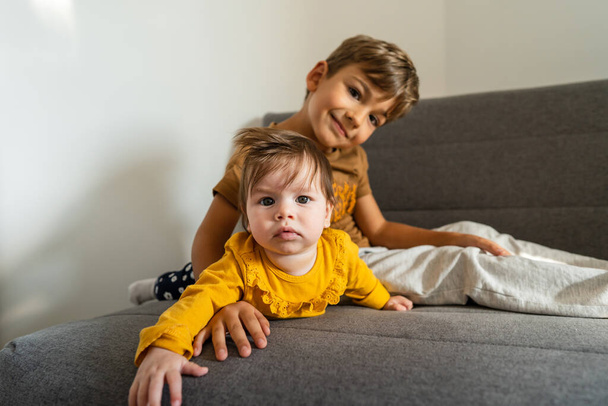 Small caucasian boy five years old lying on the bed with his baby brother or sister playing in bright room real people family bonding siblings brother and sister - 写真・画像