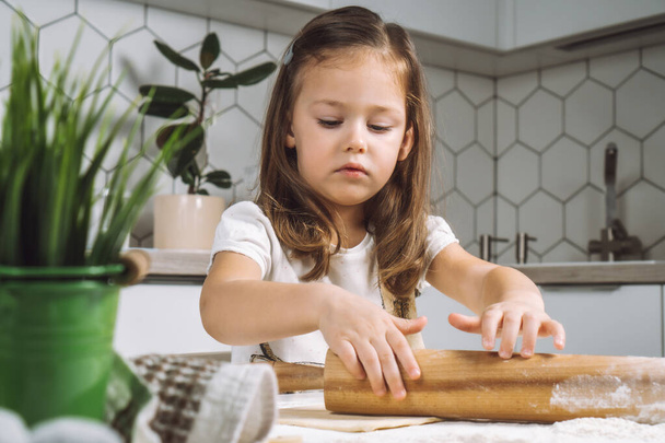 Portret małej sumiennej dziewczynki, uczącej się toczenia ciasta, robienia ciasta wielkanocnego. Trzymam mąkę z wałka. Zbliżenie - Zdjęcie, obraz