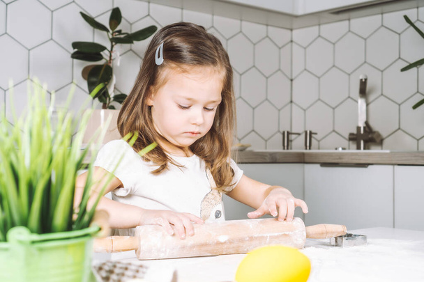 Portret małej poważnej dziewczynki, pomagającej, uczącej się toczącego się ciasta, robiącej ciasteczka wielkanocne. Trzymam wałek. Zbliżenie - Zdjęcie, obraz