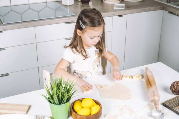 Portrait of concentrated little girl chef, sculpting dough shape cookies, baking cup. Easter holiday event preparaton - Фото, изображение