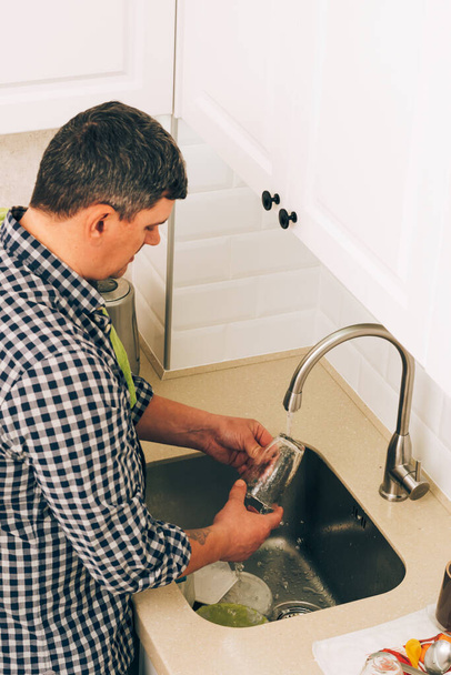 Чоловік миє посуд з миючим засобом і губкою під проточною чистою водою в раковині вдома. Стиль життя
 - Фото, зображення