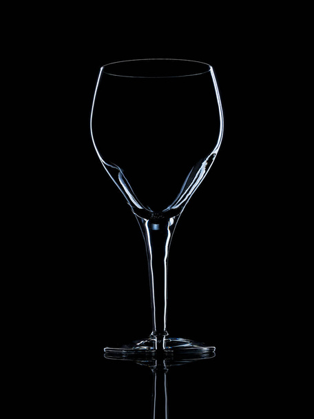 Empty crystal red wine glass on black reflective surface with rim light - Фото, изображение