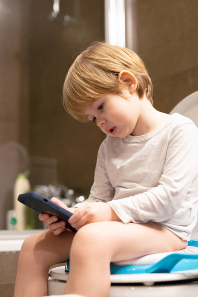 Cute toddler boy, sitting on toilet, using mobile phone. - Foto, immagini