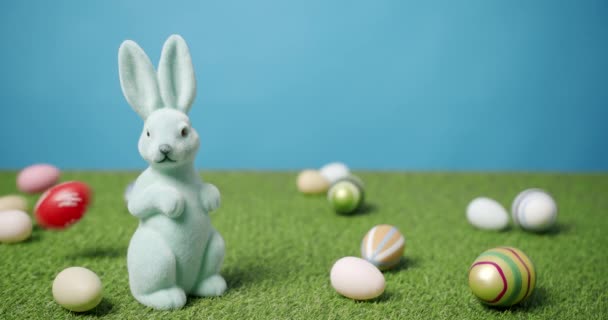 Rabbit Toy on a Blue Background of Green Grass with many colored eggs, Text. - Footage, Video