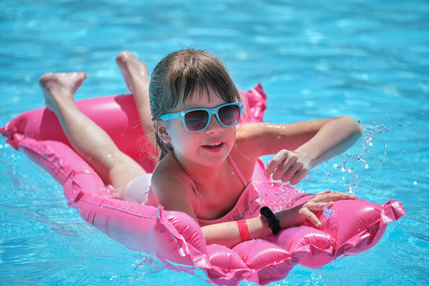 Young child girl falling in water from inflatable air mattress in swimming pool while swinnimg during tropical vacations. Safety of aquatic activities concept - Photo, Image