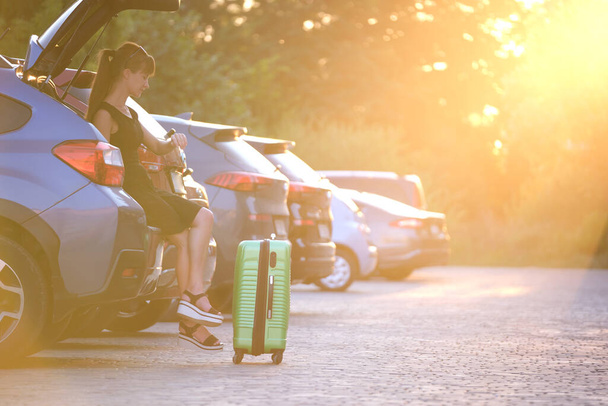 Çantalı genç bir kadın arabanın yanında bekliyor. Seyahat ve tatil kavramı - Fotoğraf, Görsel