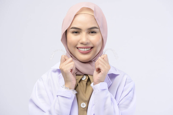 A muslim female dentist holding invisalign braces over white background studio, dental healthcare and Orthodontic concept - Photo, image